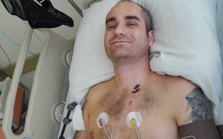 Mężczyzna leżący w szpitalnym łóżku, uśmiechający się do kamery.