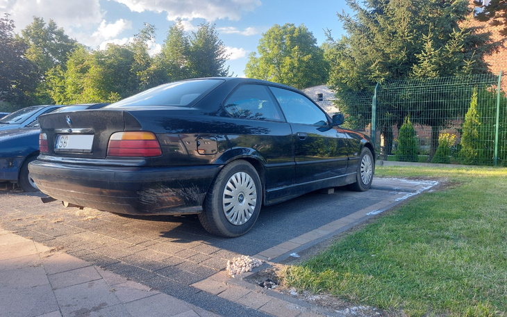 Czarny samochód zaparkowany na trawie, w tle zieleń.