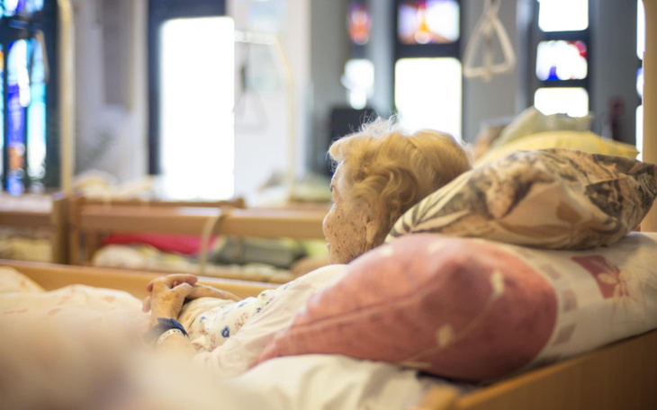 Starsza kobieta leży w łóżku w placówce opiekuńczej.