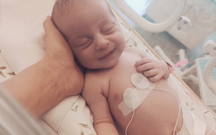 Noworodek uśmiechający się w inkubatorze, trzymany przez dorosłego.