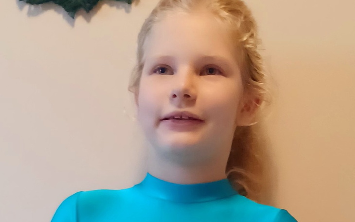 Dziewczynka w niebieskim stroju, uśmiechająca się do kamery.