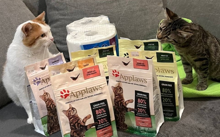 Dwa koty przy paczkach karmy, obok papier toaletowy.