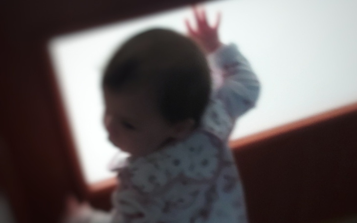 Małe dziecko dotykające szyby, z tyłu widoczna jasna przestrzeń.