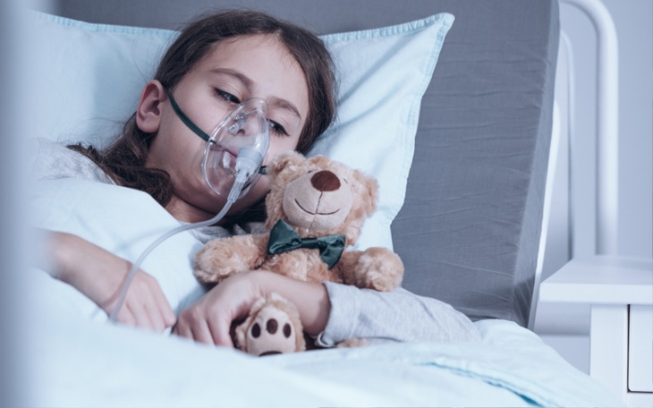 Chora dziewczynka z maską tlenową i pluszowym misiem.