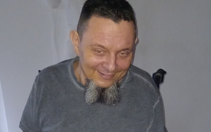 Mężczyzna uśmiechający się w szarej koszulce, siedzący na wózku.