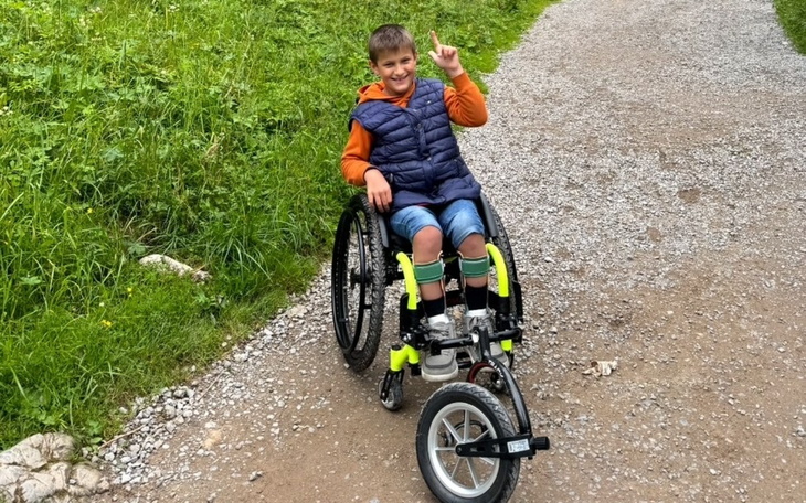 Chłopiec w wózku inwalidzkim, radośnie wskazujący palcem w górę.