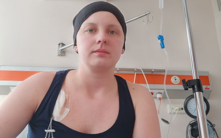 Kobieta w szpitalu, z opaską na głowie i kroplówką, patrząca w obiektyw.