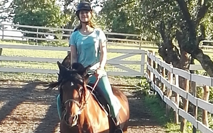 Kobieta jeżdżąca na koniu na tle zielonego krajobrazu.