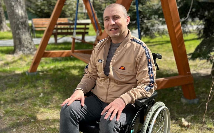 Mężczyzna na wózku inwalidzkim, uśmiechnięty w parku.
