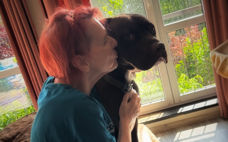 Kobieta całująca psa w słonecznym pomieszczeniu.