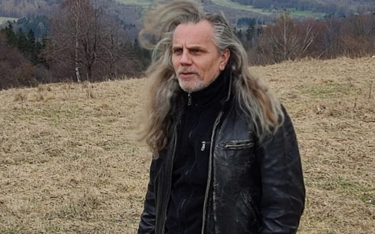 Mężczyzna z długimi włosami, stojący na łące.