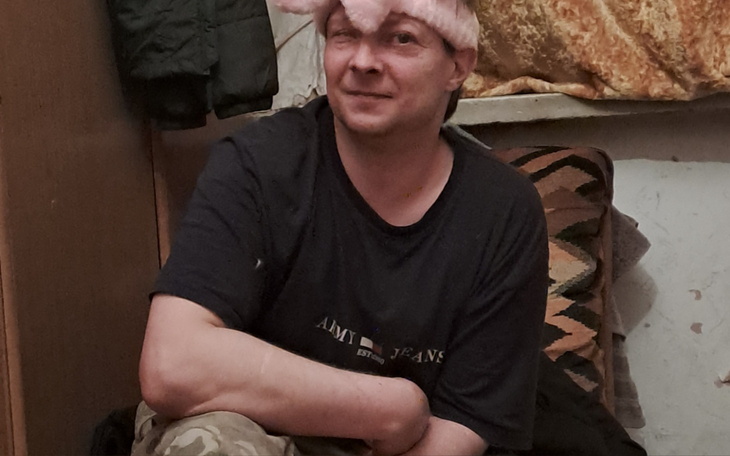 Mężczyzna w różowym kapeluszu, siedzący w pomieszczeniu.