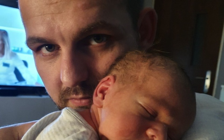 Mężczyzna trzymający śpiącego noworodka na ramieniu.