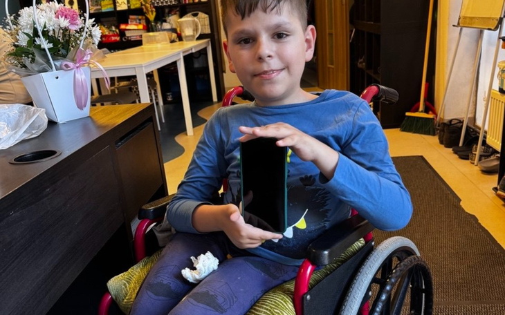 Chłopiec w wózku inwalidzkim, trzymający telefon.