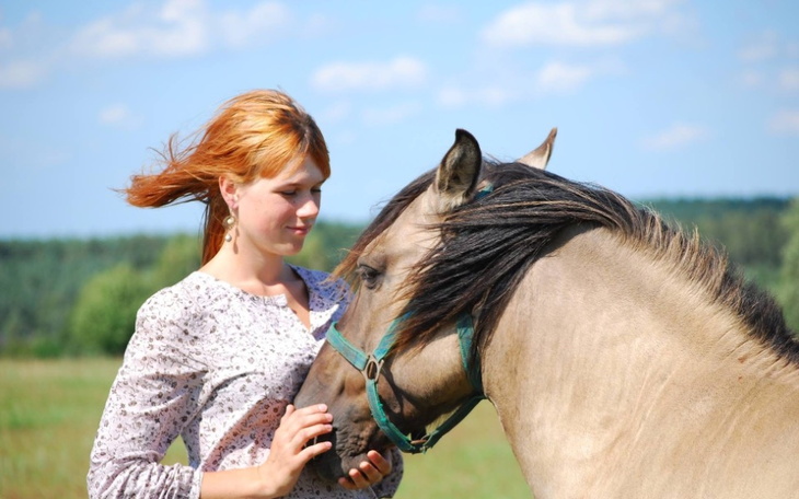 Kobieta przytulająca konia na tle zielonego krajobrazu.