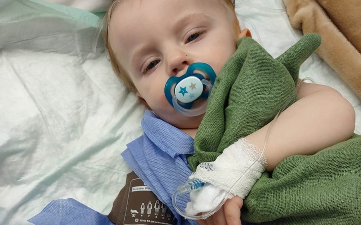 Małe dziecko w szpitalu, trzymające kocyk i smoczek.
