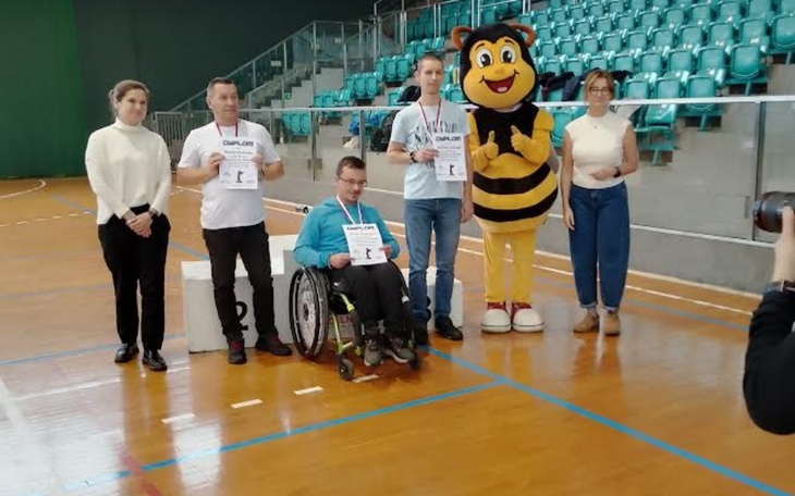Grupa ludzi z nagrodami na podium, w tle maskotka pszczoły.