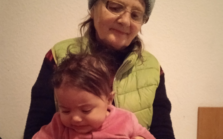 Starsza kobieta trzyma małe dziecko na kolanach, obie uśmiechnięte.