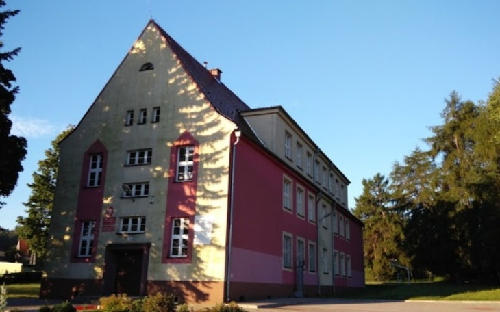 Budynek szkoły z zielonym otoczeniem i niebieskim niebem.