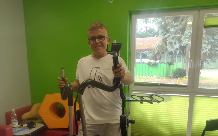 Chłopiec trzymający sprzęt rehabilitacyjny w kolorowym pomieszczeniu.