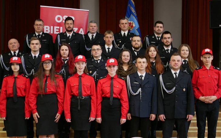 Grupa strażaków i młodzieżowa ekipa w uniformach na wydarzeniu.