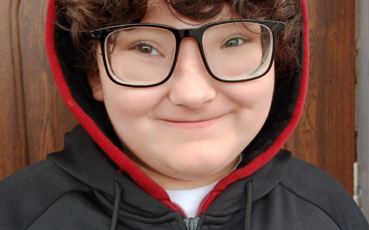 Uśmiechnięta osoba w okularach, w czarnej bluzie z kapturem.