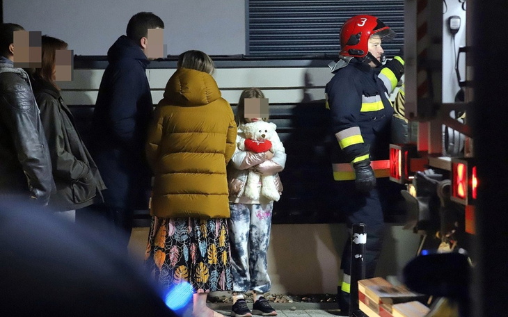 Dziecko trzymające pluszowego misia w towarzystwie strażaków.