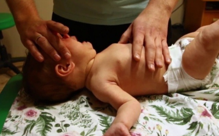 Dziecko leży na stole, a dorosły wykonuje masaż.