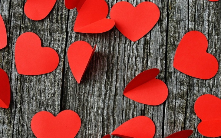 Czerwone serca z papieru rozsypane na drewnianym stole.