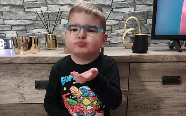 Chłopiec w okularach, całujący w powietrze, w przytulnym wnętrzu.