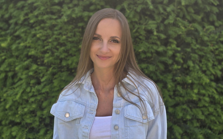 Uśmiechnięta kobieta pozująca na tle zielonego żywopłotu.