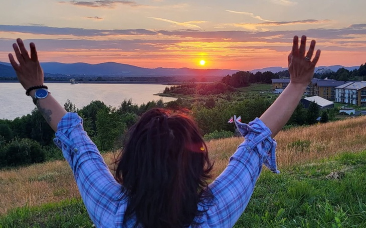 Kobieta w bluzie wita zachód słońca nad jeziorem.
