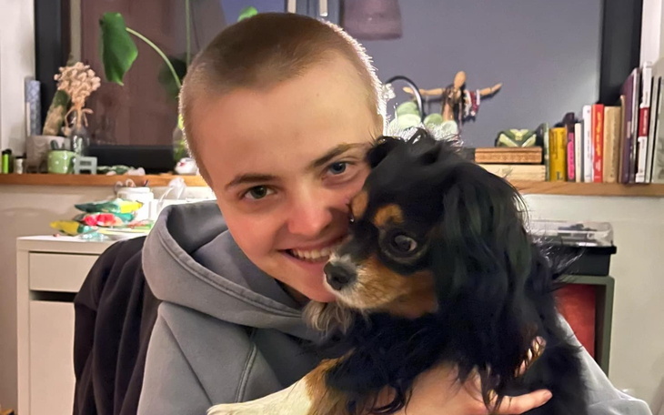 Osoba trzymająca psa, oboje uśmiechnięci w domowym otoczeniu.