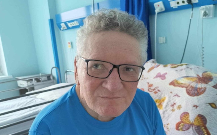 Starszy mężczyzna w szpitalu, uśmiechający się do kamery.