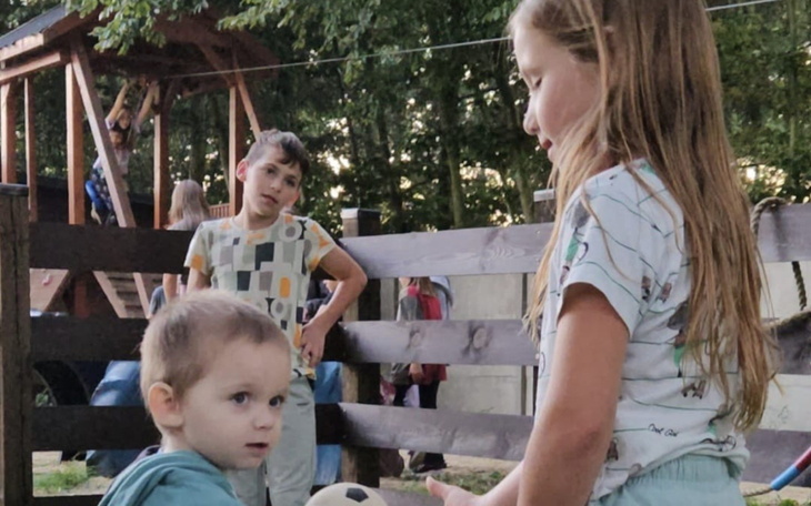 Dzieci bawiące się na placu zabaw, jedno z nich z piłką.