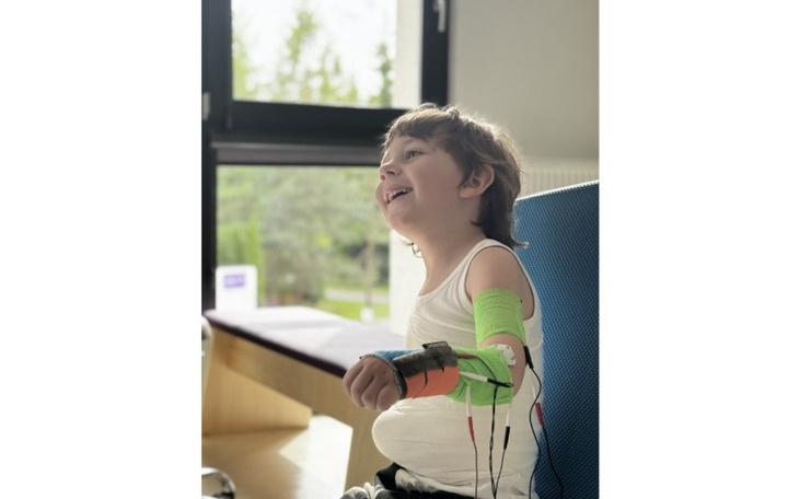 Chłopiec z uśmiechem, z urządzeniem na ramieniu.