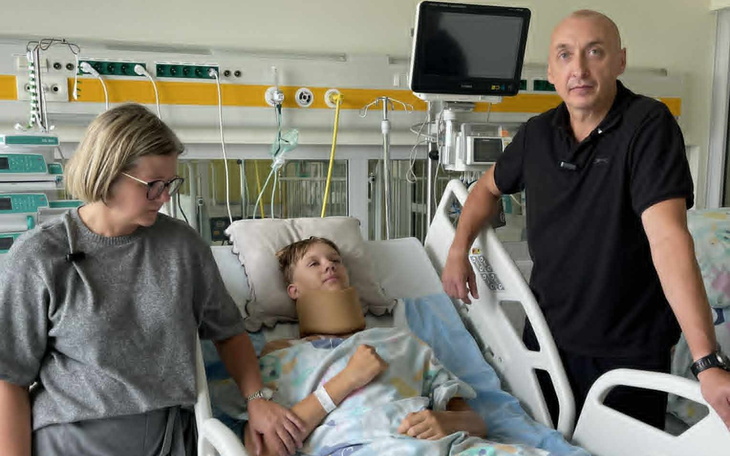 Chłopczyk z przepaską na szyi leży w łóżku szpitalnym.
