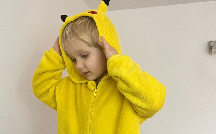 Dziecko w kostiumie Pikachu z kapturem, w zabawnej pozie.