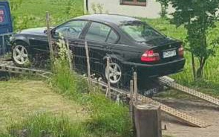 Czarny samochód na przyczepie, w otoczeniu zieleni.