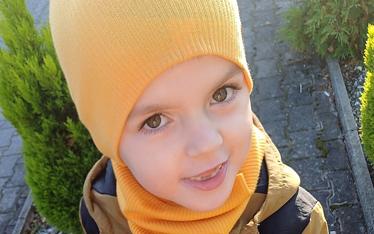 Chłopiec w żółtej czapce i szaliku, uśmiechający się do kamery.
