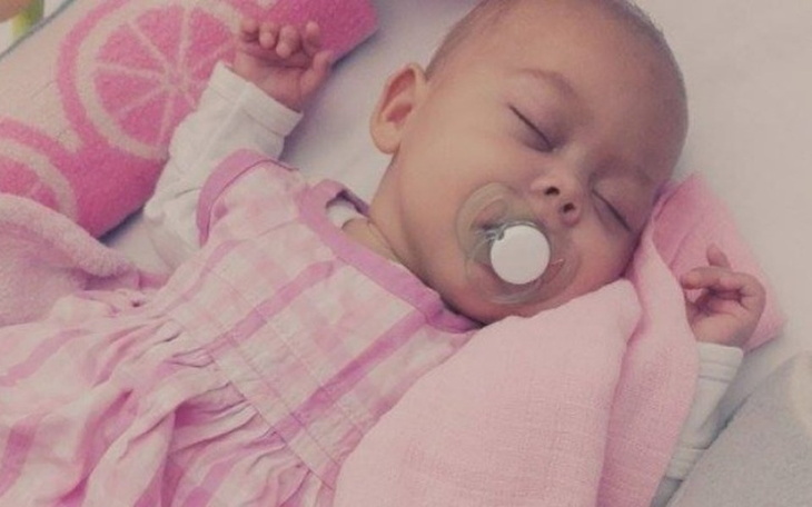 Śpiąca dziewczynka w różowej sukience z smoczkiem.