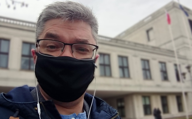 Mężczyzna w maseczce, selfie przed budynkiem.