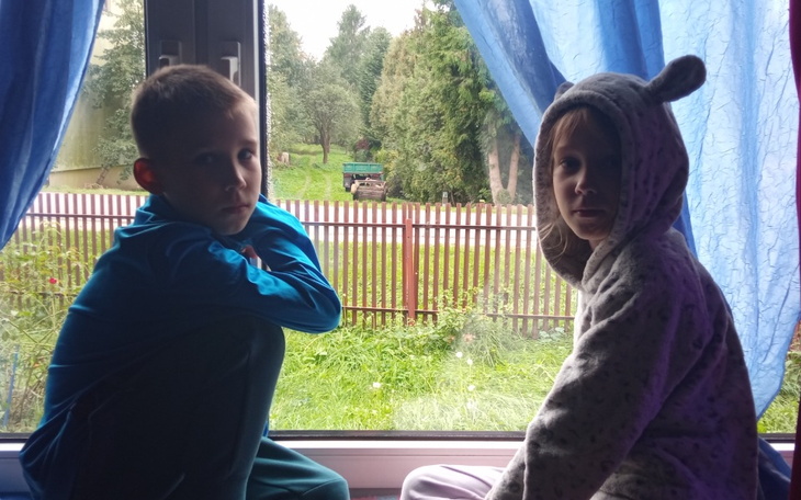 Dzieci siedzące przy oknie, z zamyślonymi minami.