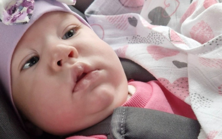 Małe dziecko w foteliku samochodowym, z różowym ubraniem i czapką.