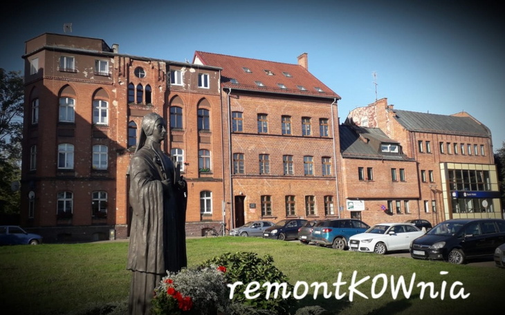 Pomnik w mieście z zabytkowymi budynkami w tle.