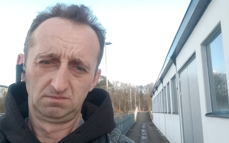 Mężczyzna z poważnym wyrazem twarzy, stojący na chodniku.