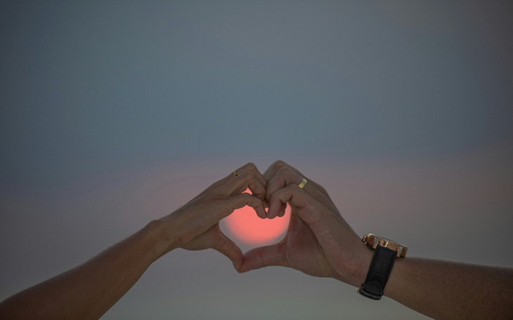 Dwie ręce tworzące serce na tle zachodzącego słońca.