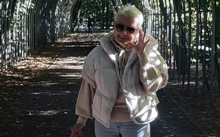 Uśmiechnięta kobieta w parku, machająca do kamery.