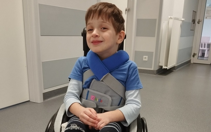 Chłopiec w wózku inwalidzkim, uśmiechający się w szpitalnym otoczeniu.