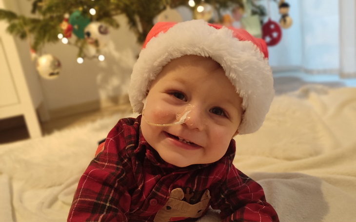 Mały chłopiec w czapce Mikołaja, uśmiechający się na tle choinki.